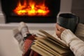 Woman with cup of hot drink and book resting near fireplace at home, closeup Royalty Free Stock Photo