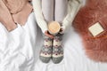 Woman with cup of hot drink wearing knitted socks on fabric, top view. Warm clothes