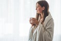 Woman with cup of hot drink by the window. Looking at window and drink tea.