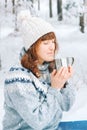 Woman with a cup of tea in her hands siting in in snow-covered forest