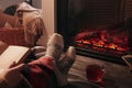 Woman with cup of tea reading book near fireplace at home, closeup Royalty Free Stock Photo