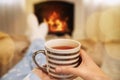 Woman with cup of tea resting near fireplace at home, closeup Royalty Free Stock Photo