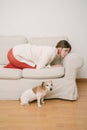 Woman curled up on beige sofa and dog on floor looking at camera.