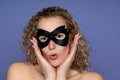 Woman with curly hair and bare shoulders, with a black face mask, she is surprised and touched her face