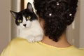 Woman with curly hair holding domestic black and white kitten with green eyes. Concept of love to animals, pets, lifestyle, care.