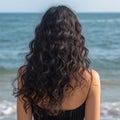 A woman with curly hair stands with her back in the wind on the beach.