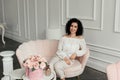 Woman with curly hair in a white blouse sits on a pink sofa