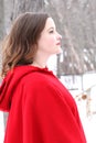 Woman with curly, long hair in vintage red cape looks forward in outdoor winter scene