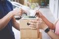 Woman customer appending signature in digital tablet and receiving a cardboard boxes parcel from delivery service courier, Home