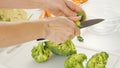 Woman cuts broccoli on a white cutting board. Fresh raw organic vegetables close-up on the kitchen table. Vegetable soup or salad Royalty Free Stock Photo