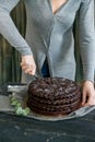 Woman cuts chocolate cake close. Dark tones