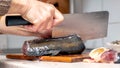 A woman cuts fish with a large knife at home in the kitchen