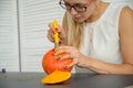 A woman cuts out a face with a stationery knife on a pumpkin for Halloween lamps on a black table. Close-up of female