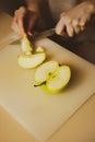 A woman cuts a ripe green apple on the kitchen table with a sharp knife. Home cooking. Healthy nutrition. Fruit diet and