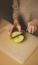 A woman cuts a ripe green apple on the kitchen board with a sharp knife. Fresh fruit. Healthy nutrition. Diet