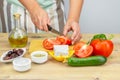 Woman cuts tomatoes for Greek salad. Ingredients for Greek Salad on wooden background. Healthy food, Mediterranean diet. Girl cook