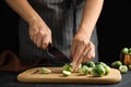 Woman cutting Brussels sprout at black slate table, closeup