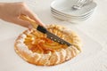 Woman cutting delicious peach galette on board, closeup