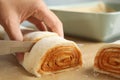 Woman cutting dough for cinnamon rolls on parchment at table