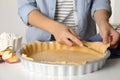 Woman cutting dough leftovers for traditional English apple pie in baking dish at white table, closeup