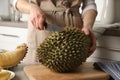 Woman cutting durian at table in kitchen, closeup