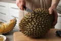 Woman cutting durian at table in kitchen, closeup