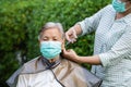 Woman cutting female senior hair during coronavirus or covid 19 out break in self quarantine with mask