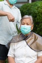 Woman cutting female senior hair during coronavirus or covid 19 out break in self quarantine with mask