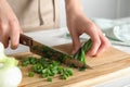 Woman cutting fresh green onion on wooden board at table Royalty Free Stock Photo