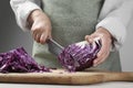 Woman cutting fresh radicchio cabbage on board at wooden table, closeup