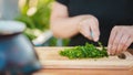 Woman cutting greens on wooden board outdoors. Close up of woman& x27;s hands cutting verdure with knife on chopping board. Royalty Free Stock Photo