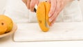 Woman cutting mango on white cutting board, preparing fruit salad Royalty Free Stock Photo