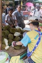 Woman cutting up Durian fruit watched by customers on Khong Toei wet market in Bangkok, Thailand