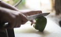 Woman cutting whole green capsicum with a knife on a chopping board in an Indian kitchen Royalty Free Stock Photo