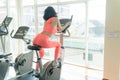 Woman cycling exercise in the gym. Back view of attractive beautiful woman wearing orange sportswear on exercise