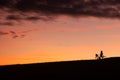 Woman cyclist pushing her bike uphill. After sunset silhouette, unrecognizable. Bicycle has toddler child seat