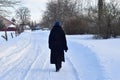 A woman in dark clothes walks along a road that is white with snow. Royalty Free Stock Photo