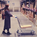 A woman in dark clothing and a medical mask stands with a cart in the warehouse