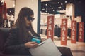 Woman in dark glasses sitting in mall walking zone holding back of credit card and white paper shopping bag at sale signs Royalty Free Stock Photo