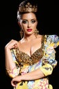 Woman with dark hair in luxurious gold dress with bijou and crown,