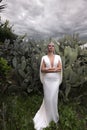 woman with dark hair in luxurious wedding dress with jewelry posing in beautiful nature place Lefkara, with cactus plantation in