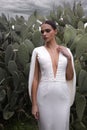 woman with dark hair in luxurious wedding dress with jewelry posing in beautiful nature place Lefkara, with cactus plantation in