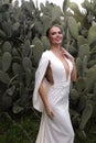 woman with dark hair in luxurious wedding dress with jewelry posing in beautiful nature place Lefkara, with cactus plantation in