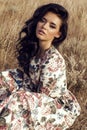 Woman with dark hair wears luxurious colorful dress posing in summer field