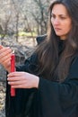 Woman with dark long hair in black robes is holding red burning candle in her hands in the middle of the forest Royalty Free Stock Photo