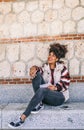 Woman with dark skin and afro hair sitting on a stone bench, smiles while she is thinking something to write in her notebook Royalty Free Stock Photo