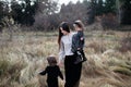 Woman with daughter in her arms and son near them on dry grass field and forest background. Royalty Free Stock Photo