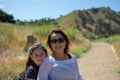 Woman and daughter walking together on a trail or dirt road in the woods next to a yellow field