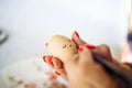 Woman decorate an easter egg preparing for celebration of a holiday. Female hand brushes, painting and drawing little face on an