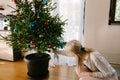 A woman decorates a live Christmas tree in a flower pot.